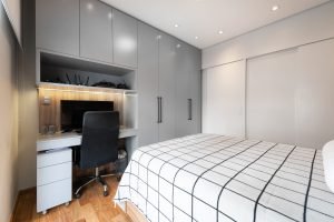 Quarto dormitório solteiro com armários cinza e madeira. Adaptamos o armário para criair uma bancada de estudo e home office.